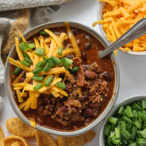 Hearty serving of chili with bacon in a bowl, garnished with green onions and shredded cheese