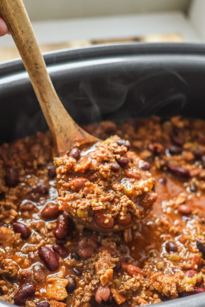 Hearty spoonful of bacon chili in a ladle, ready to be served into a bowl with rich, flavorful broth and chili beans.