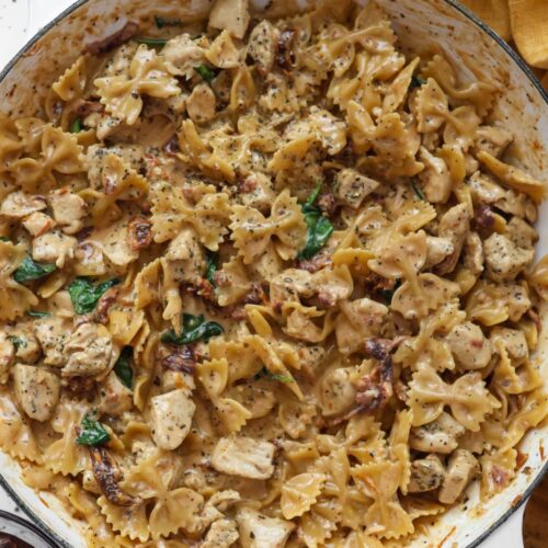 A delicious serving of Tuscan chicken pasta in a cast iron skillet, with creamy sauce, sun-dried tomatoes, and wilted spinach