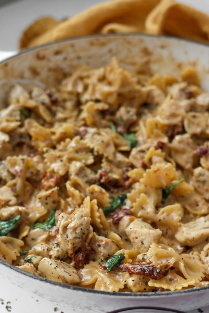 Close-up of creamy Tuscan chicken pasta in a skillet, with golden-brown chicken, wilted spinach, and vibrant sun-dried tomatoes.