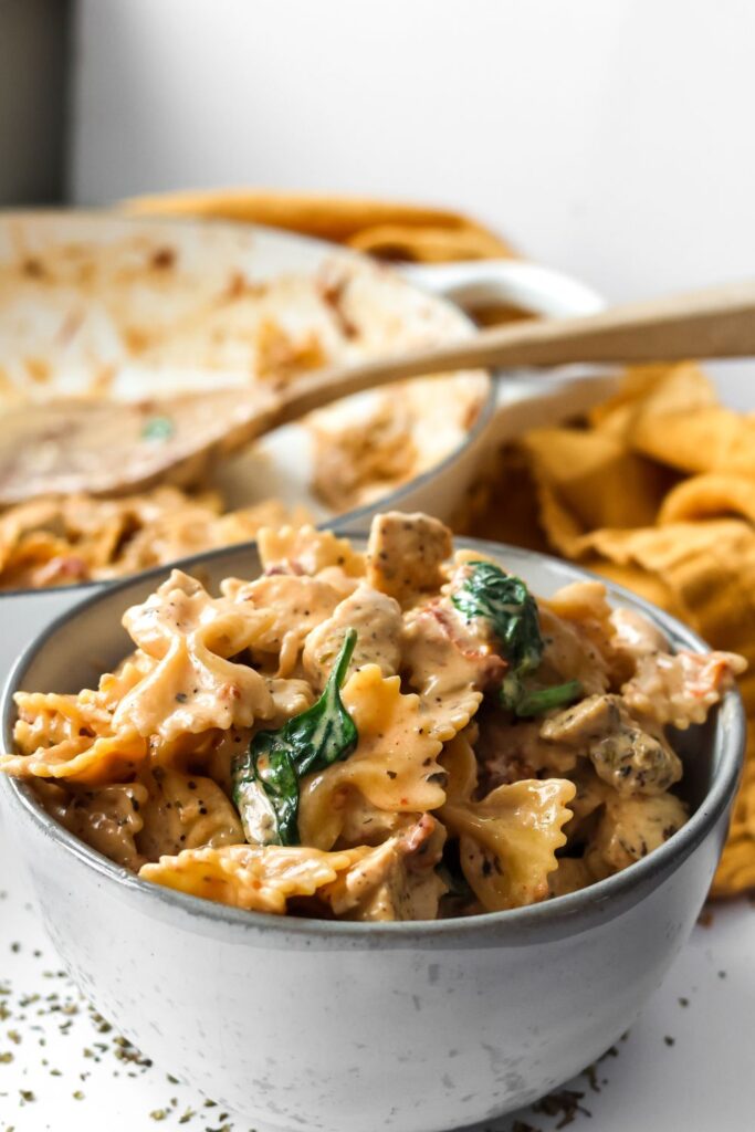 A bowl of Tuscan chicken pasta, with bowtie pasta, creamy sauce, spinach, and sun-dried tomatoes