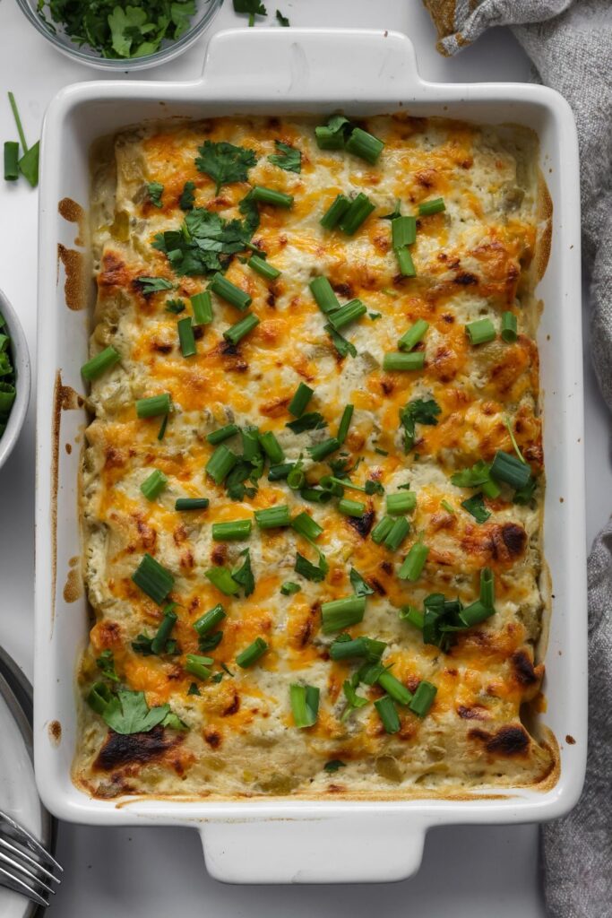 white casserole dish filled with chicken enchiladas and sour cream sauce, cilantro and green onions