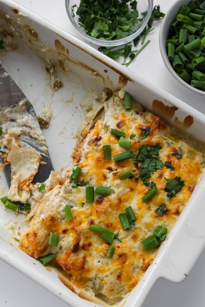 a casserole dish with 3 enchiladas in that are covered with a white sour cream sauce, cilantro and green onions. 