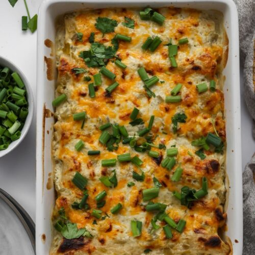 A casserole dish filled with golden-brown, cheesy white chicken enchiladas, topped with fresh cilantro and a creamy white sauce