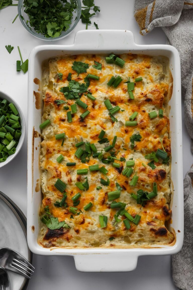 A casserole dish filled with golden-brown, cheesy white chicken enchiladas, topped with fresh cilantro and a creamy white sauce