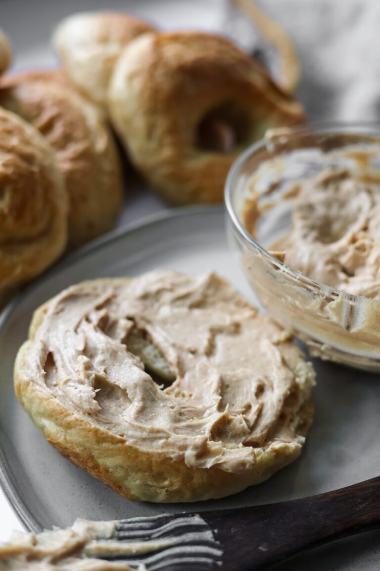 A toasted bagel generously spread with creamy brown sugar cinnamon cream cheese on a white plate.