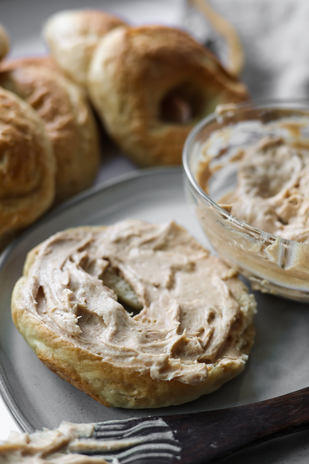 A toasted bagel generously spread with creamy brown sugar cinnamon cream cheese on a white plate.