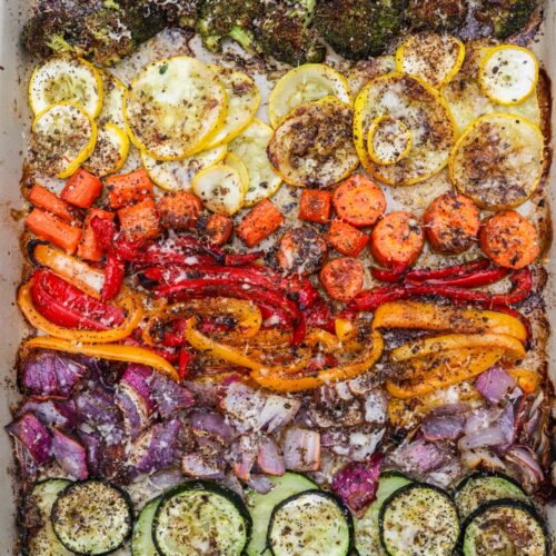 A large sheet pan filled with oven-roasted vegetables, including baby carrots, zucchini, and yellow squash, cooked to perfection with a crispy parmesan topping.