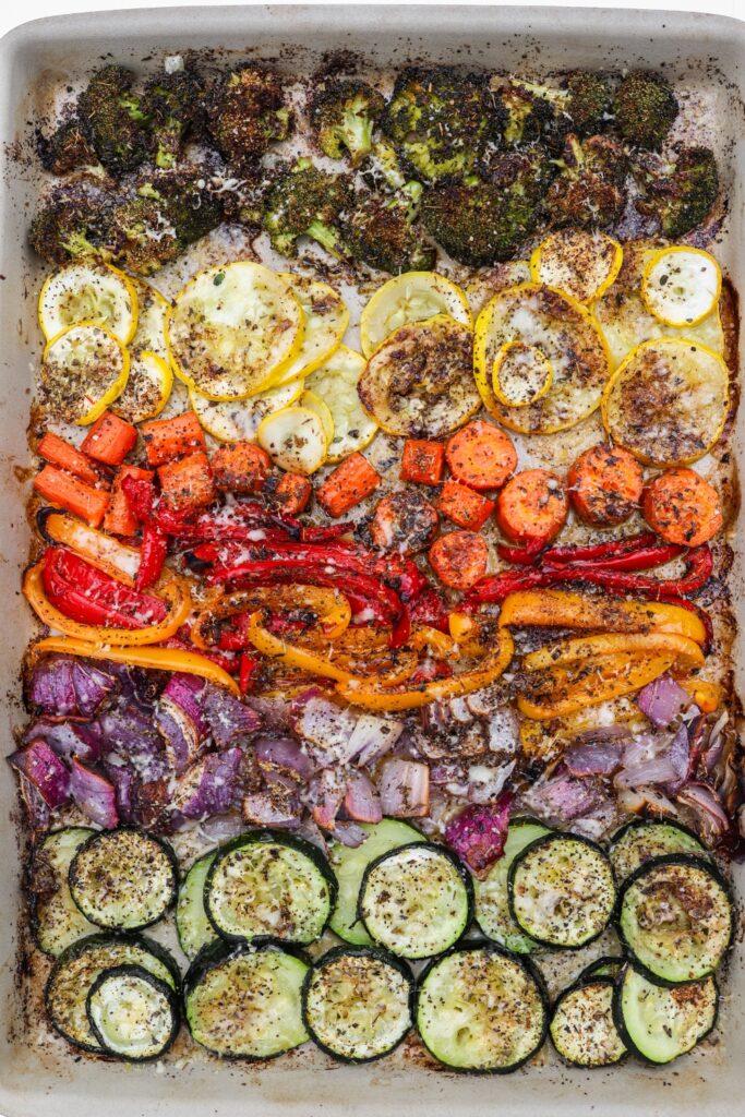 A large sheet pan filled with oven-roasted vegetables, including baby carrots, zucchini, and yellow squash, cooked to perfection with a crispy parmesan topping.