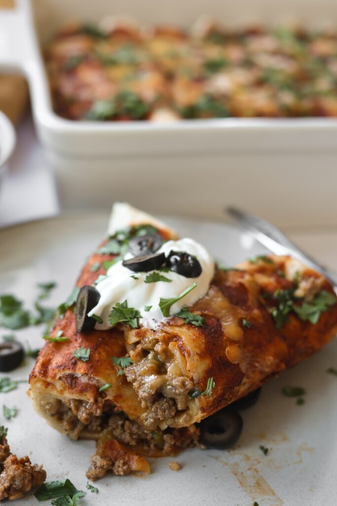 a ground beef enchilada cut in half so you can see the ground beef mixture on the inside.