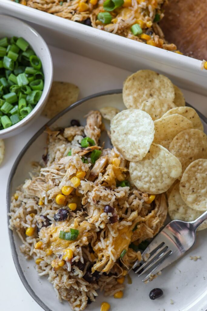 A serving of Chicken Burrito Casserole on a plate, topped with shredded cheese, green onions.