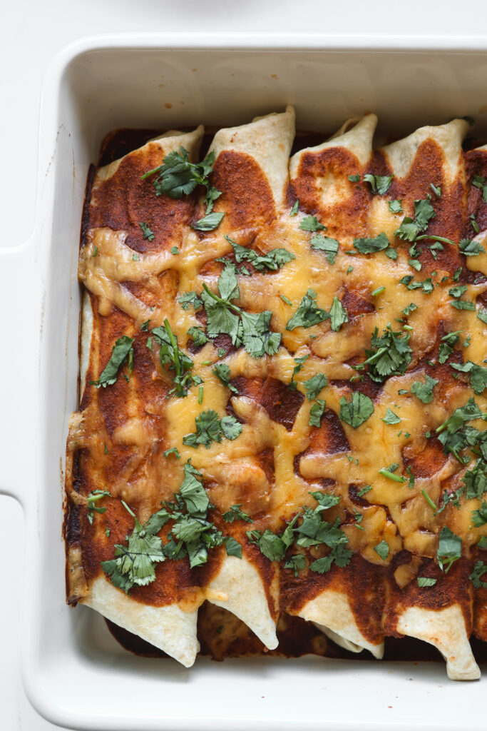 an overhead view of 4 ground beef enchiladas rolled up in a 9x13 casserole dish with red sauce, cheese and cilantro sprinkled on top