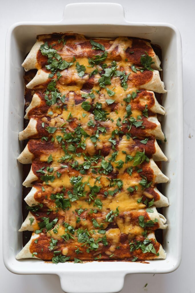 an overhead photo looking down on a 9x13 casserole dish filled with ground beef enchiladas rolled up in flour tortillas with red sauce, cheese and cilantro