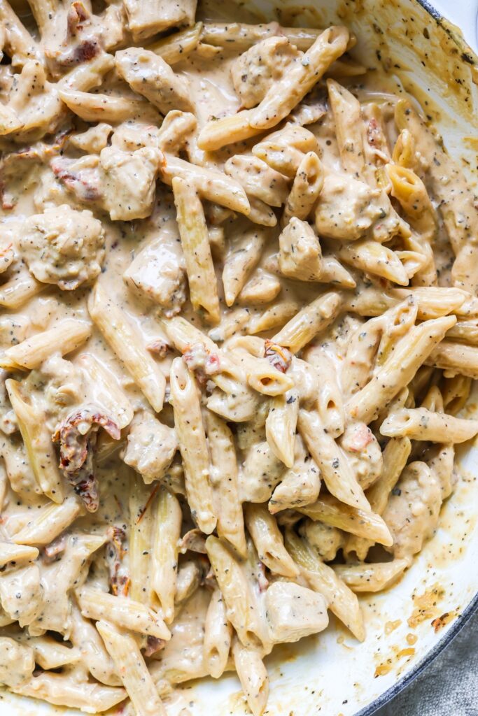 Close-up of Marry Me Chicken Pasta in an enameled cast iron skillet, featuring pasta, chicken, and a rich creamy sauce with a sprinkle of Parmesan.